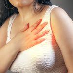 Woman suffering from chest pain on a gray background. Health care concept.